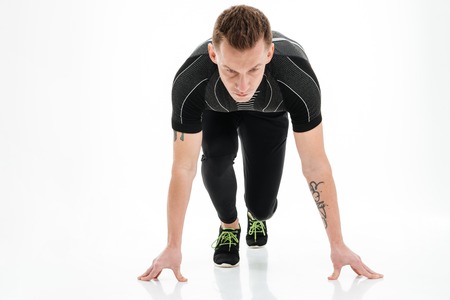 Portrait of a focused young male sprinter preparing to start running isolated over white backgroundの写真素材