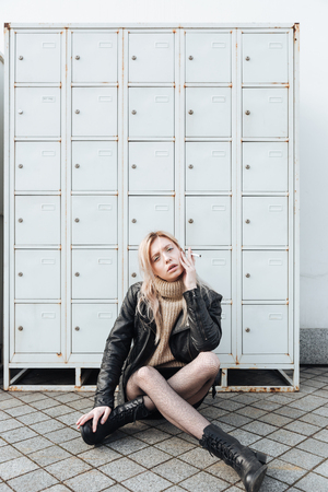 Fashion portrait of serious young blonde lady sitting near safes. Looking at camera holding cigarette.の写真素材
