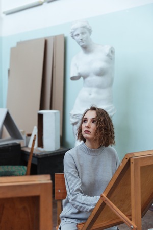 Young woman painting or drawing while sitting at an easel in a classroomの写真素材