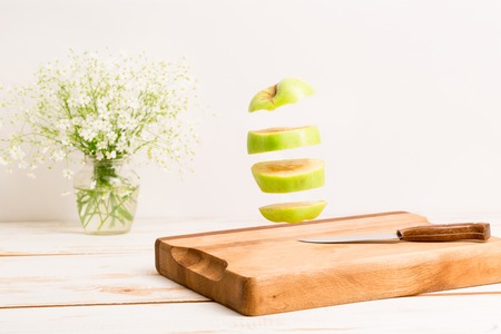 Sliced whole green apple flying above a wooden chopping board with a knifeの写真素材