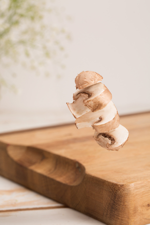 Close up of a sliced whole mushroom flying above a wooden chopping board with vase of flowersの写真素材