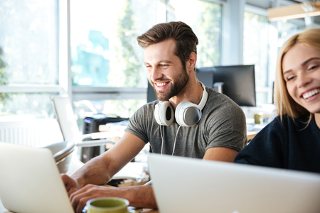Photo of cheerful young colleagues sitting in office coworking using laptop computers. Looking aside.の写真素材