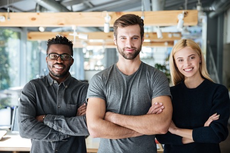 Image of smiling young colleagues in office coworking standing with arms crossed. Looking at camera.の写真素材
