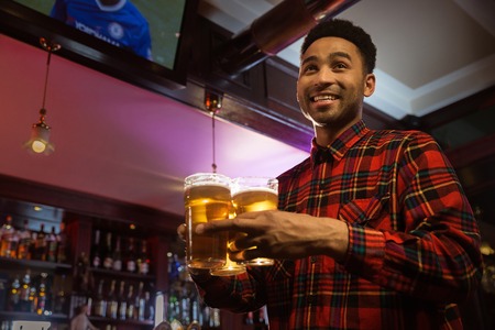 Smiling afro american man carrying glasses of beer in a pub or barの写真素材