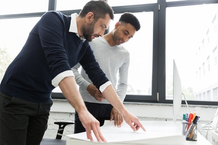 Two young male office workers pointing on a chart on a desk while standingの写真素材