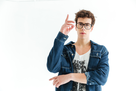 Hipster in eyeglasses and jeans clothes posing in studio and looking at the camera over white backgroundの写真素材