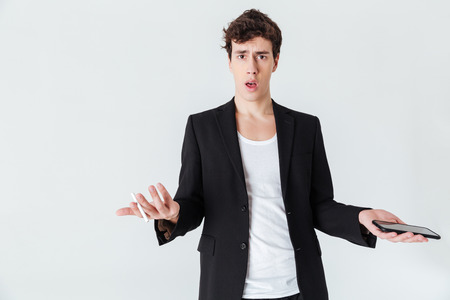 Shocked Man in suit holding cigarette and  smartphone while looking at the camera over white backgroundの写真素材