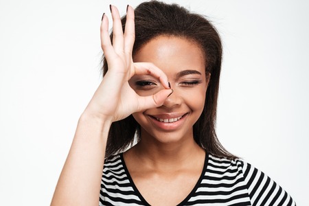 Image of happy young african lady standing isolated over white background. Showing okay gesture while looking at camera.の写真素材