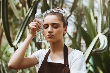 Image of concentrated young woman standing in greenhouse holding water. Eyes closed.の写真素材