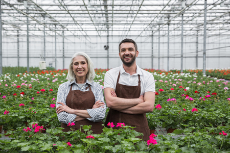 Image of young cheerful man standing in greenhouse near mature woman and plants. Looking aside.の写真素材