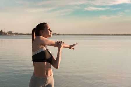 Picture of young sports woman at the beach make stretching exercises.