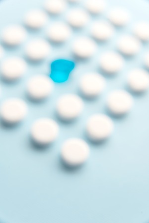 One blue liquid capsule in a grid of white tablets isolated. Close up unfocusedの写真素材