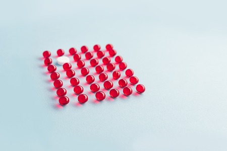 One white round tablet in a grid of red liquid capsules isolatedの写真素材