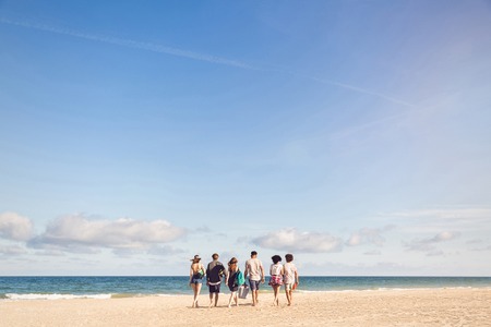Rear view portrait of group of young people walking on the beach carrying a cooler boxの写真素材