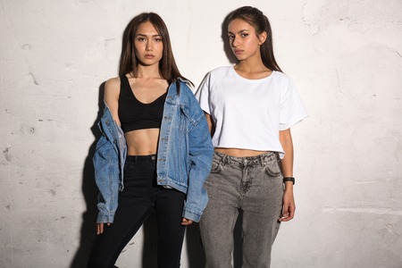 Picture of concentrated young hipsters ladies standing over gray background.