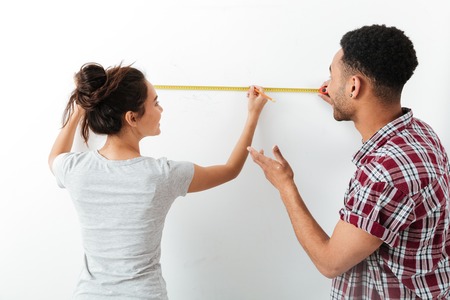 Happy young couple standing and using measuring tape over white backgroundの写真素材