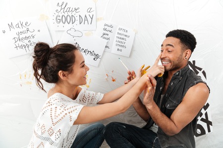 Image of happy young loving couple artists sitting on floor over white background. Looking aside.の写真素材