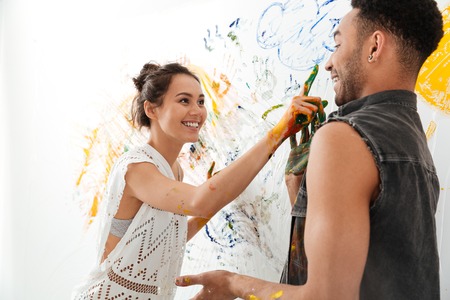 Cheerful young couple painting with brushes by hands and having funの写真素材