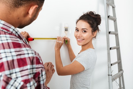 Cheerful yong couple using brush and measuring tape over white background
