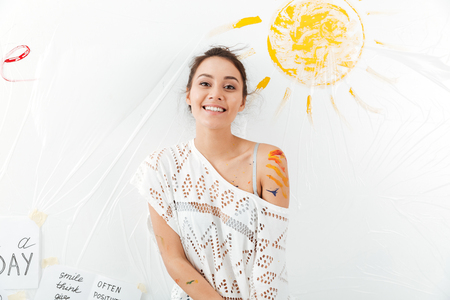 Happy attractive young woman standing over white background with painted yellow sunの写真素材