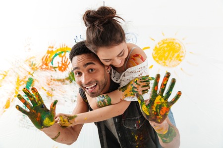 Smiling young couple painting with brushes by hands and hugging over white backgroundの写真素材