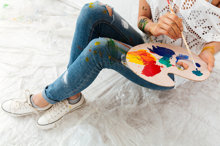 Closeup of woman sitting and painting with brush and colorful paints on palette over white backgroundの写真素材