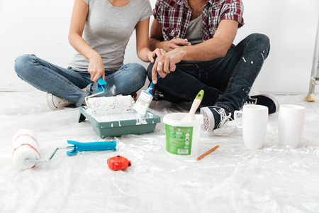 Cropped photo of young loving couple sitting on floor in new flat makes repair.の写真素材