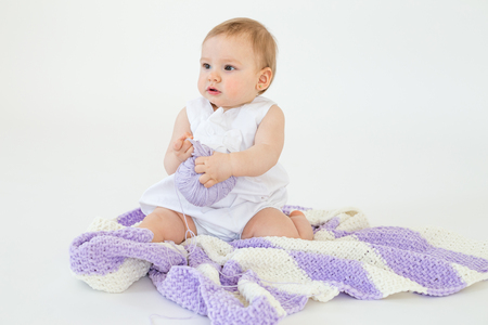 Picture of little baby girl sitting on floor with plaid isolated over white background playing with threads ball. Looking aside.の写真素材