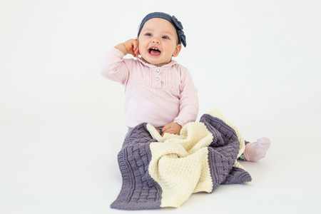 Photo of cheerful girl sitting on floor with plaid isolated over white background. Looking aside.