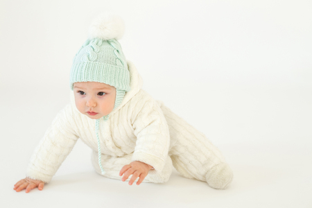 Image of cute little baby wearing hat sitting on floor over white background. Looking aside.の写真素材