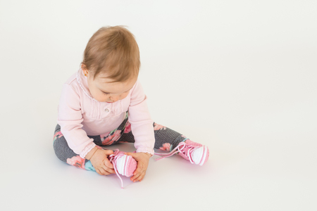 Photo of cute little baby girl sitting on floor isolated over white background. Looking aside.の写真素材
