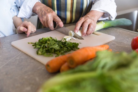 Close up of a senior lady cutting vegetables on a board with her granddaughter at the kitchenの写真素材