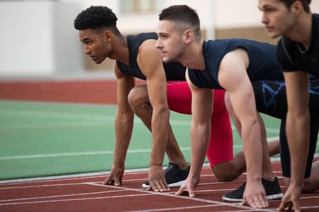 Image of concentrated multiethnic athlete group ready to run on running track outdoors. Looking...
