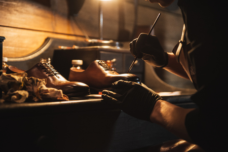 Cropped image of young concentrated man shoemaker at footwear workshop.