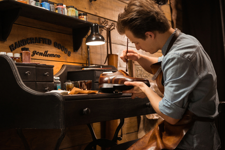 Picture of young concentrated shoemaker in workshop making shoes. Looking aside.の写真素材