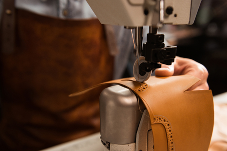 Close up of a shoemaker using sewing machine in workshopの写真素材