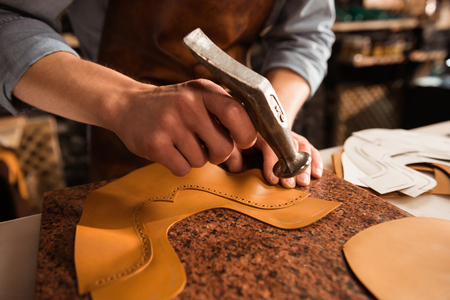Close up of a shoemaker man working with leather using hammer