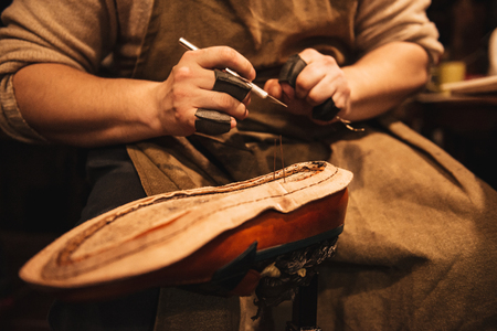 Cropped photo of young man shoemaker at footwear workshop.