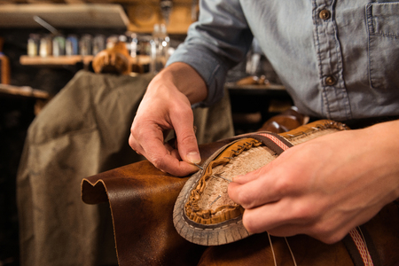 Cropped image of bootmaker sitting in workshop making shoes