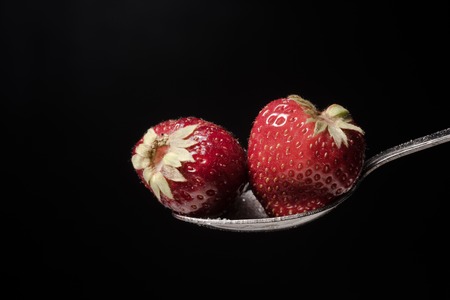 Spoon with strawberry isolated over black background.の写真素材