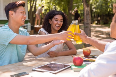 Picture of cheerful young multiethnic friends students outdoors drinking juice and talking with each...