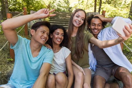 Image of young happy multiethnic friends students outdoors make selfie by mobile phone and talking with each other. Looking aside.の写真素材