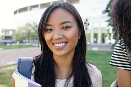 Picture of young happy student asian woman standing outdoors. Looking camera.