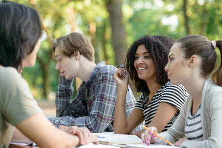 Image of multiethnic group of happy young students sitting and studying outdoors while talking. Looking aside.の写真素材