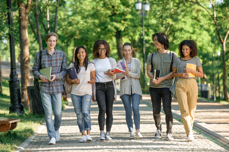 Picture of multiethnic group of young cheerful students walking while talking. Looking aside.の写真素材
