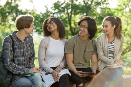 Picture of multiethnic group of young cheerful students sitting and studying outdoors. Looking aside.の写真素材