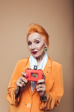 Photo of amazing mature redhead fashion woman standing isolated at studio and holding camera....