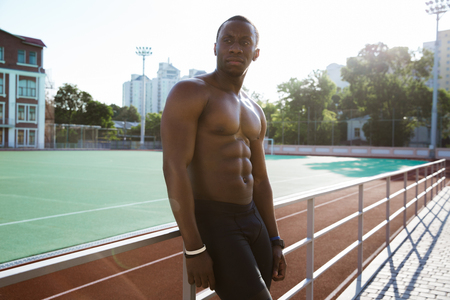 Young tired african athlete man resting while leaning on a railing at the stadiumの写真素材