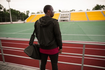 Back view of a young african sportsman with bag standing at the open stadiumの写真素材