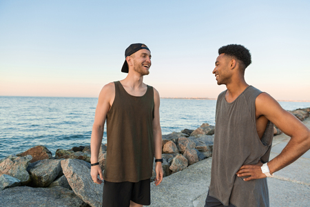 Two smiling young guys in sportswear talking while standing outdoorsの写真素材
